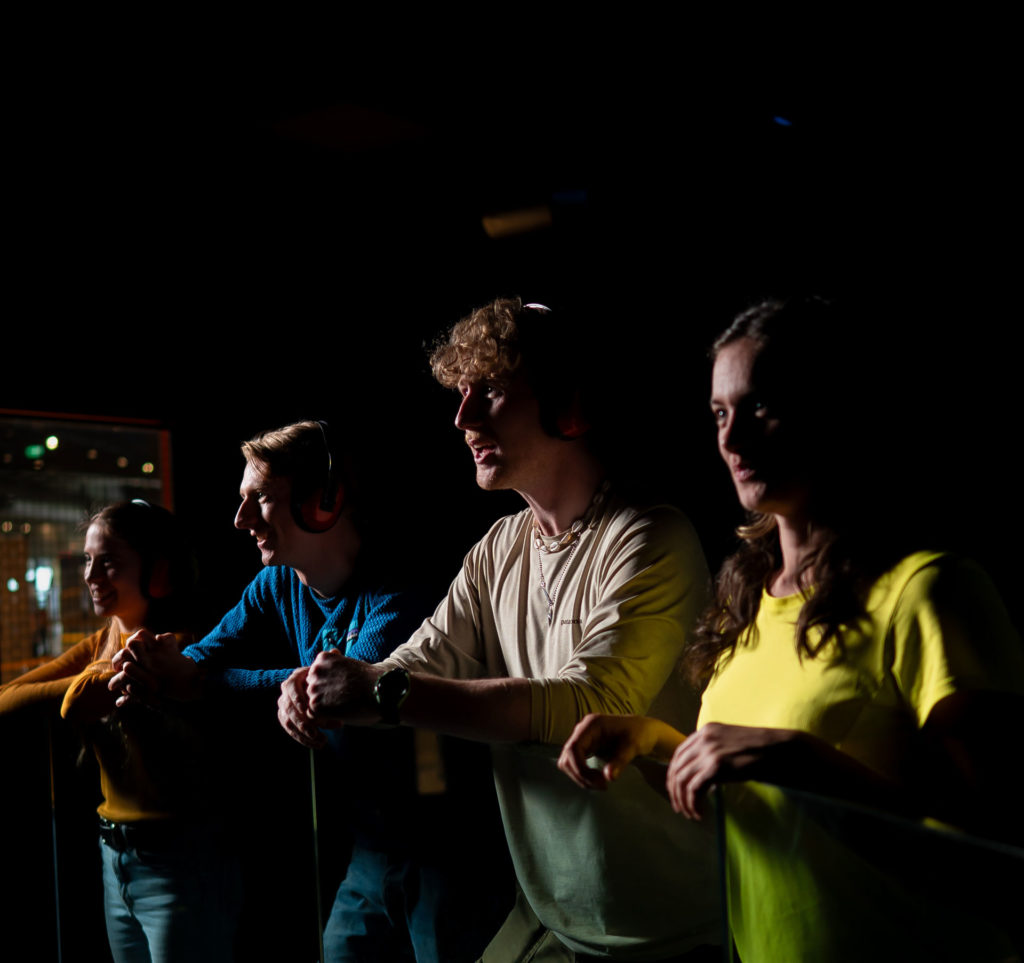 Four people in headphones chatting in a dimly lit space, each wearing colorful shirts, enjoying a lively conversation.
