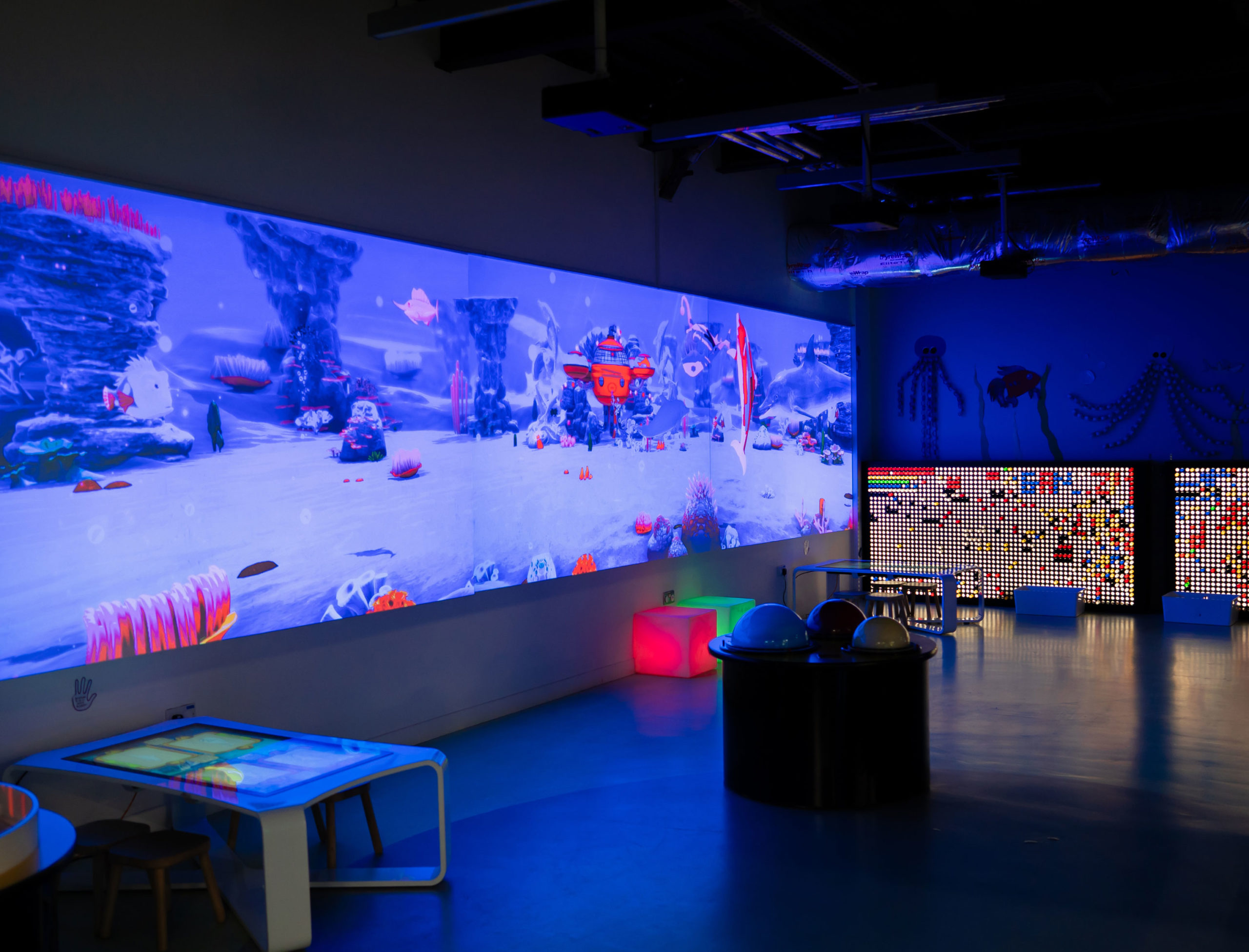 Interactive children's playroom with vibrant underwater-themed digital screens and colorful seating.