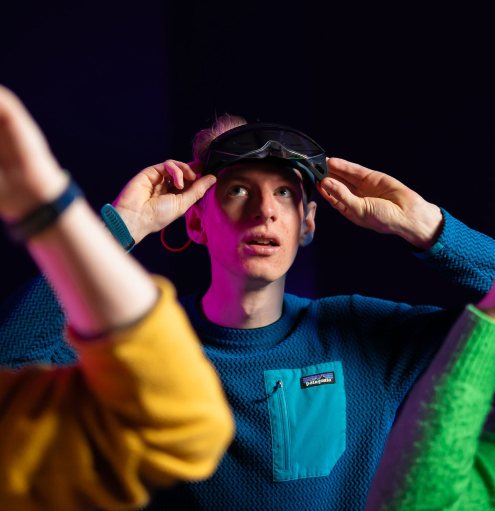 Person adjusting VR headset in vibrant lighting, wearing a blue top.