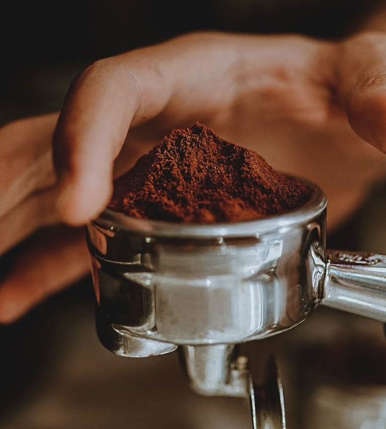 Hand holding portafilter with freshly ground coffee, ready for brewing espresso.
