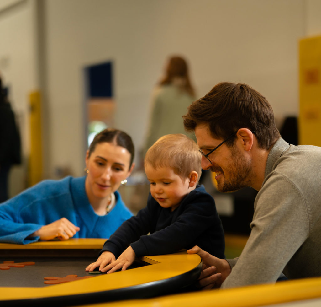 Family enjoying playful learning at a table game with toddler in an indoor setting.