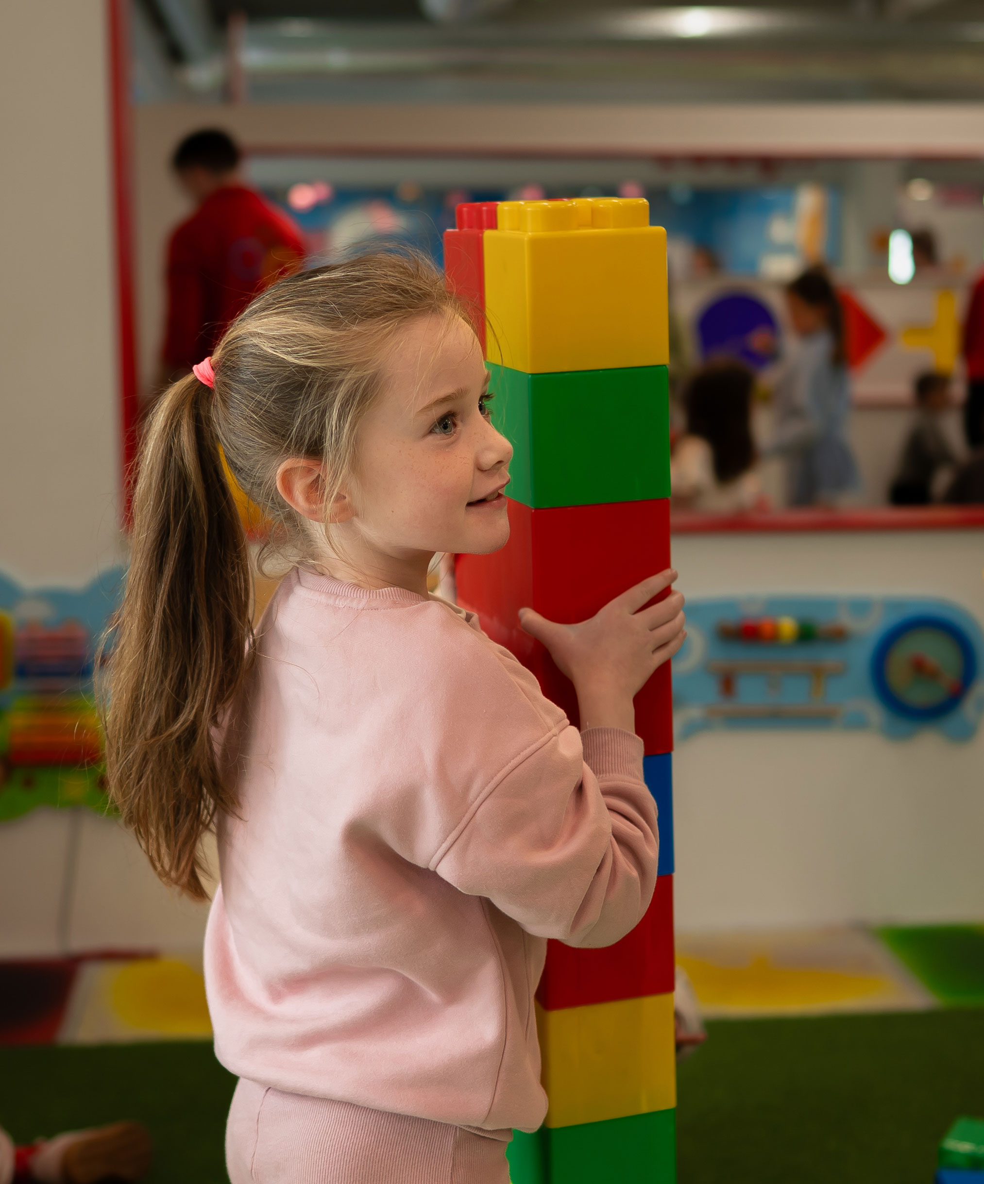 Girl playing with large colorful building blocks indoors at a children's play area.