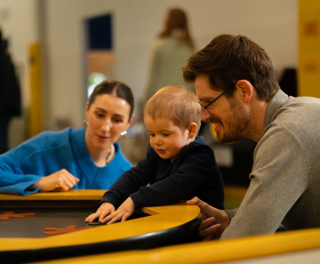 Parents engaging with child in a playful learning activity at a table, fostering creativity and development.