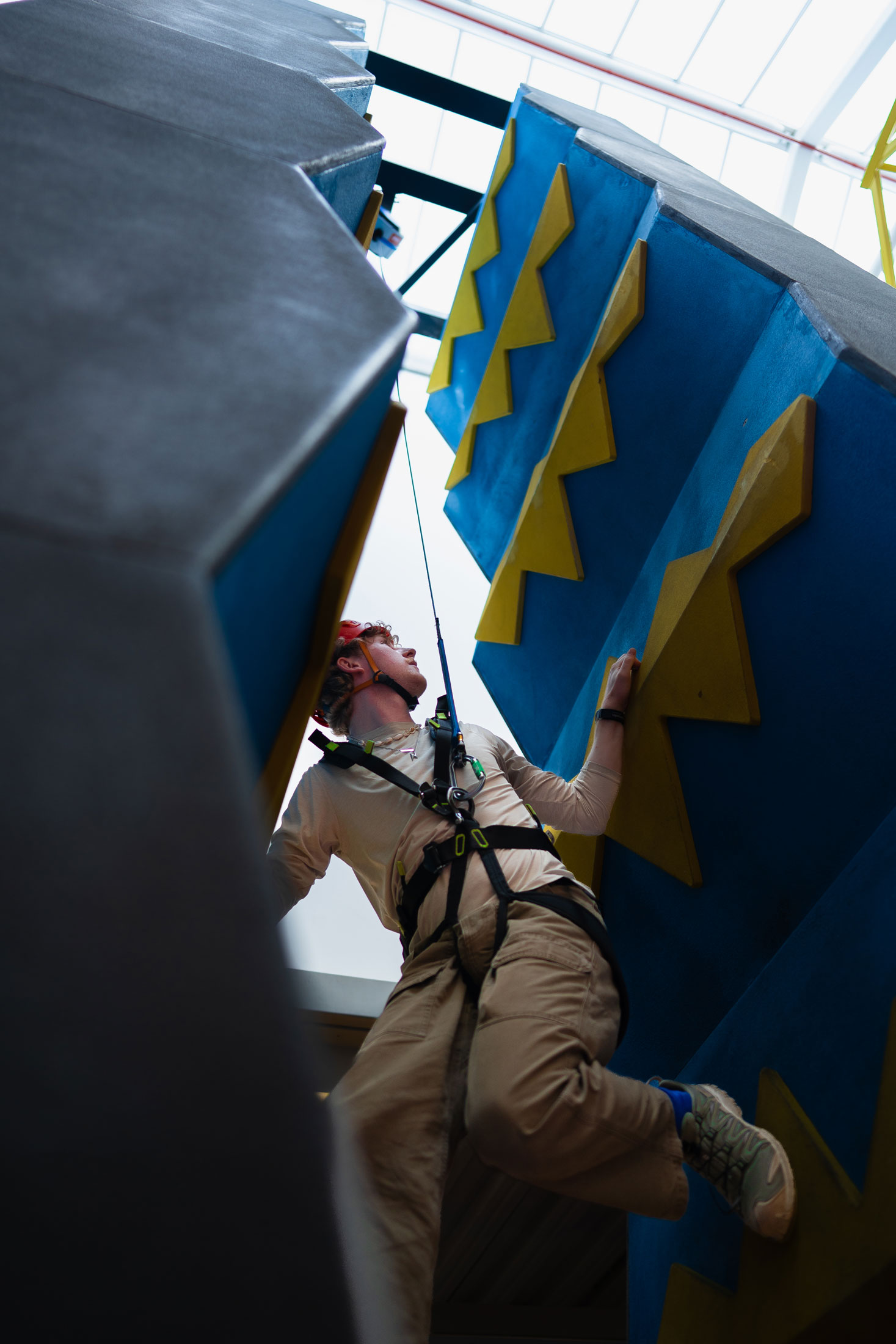 Person scaling indoor rock climbing wall with harness, wearing helmet, in action.