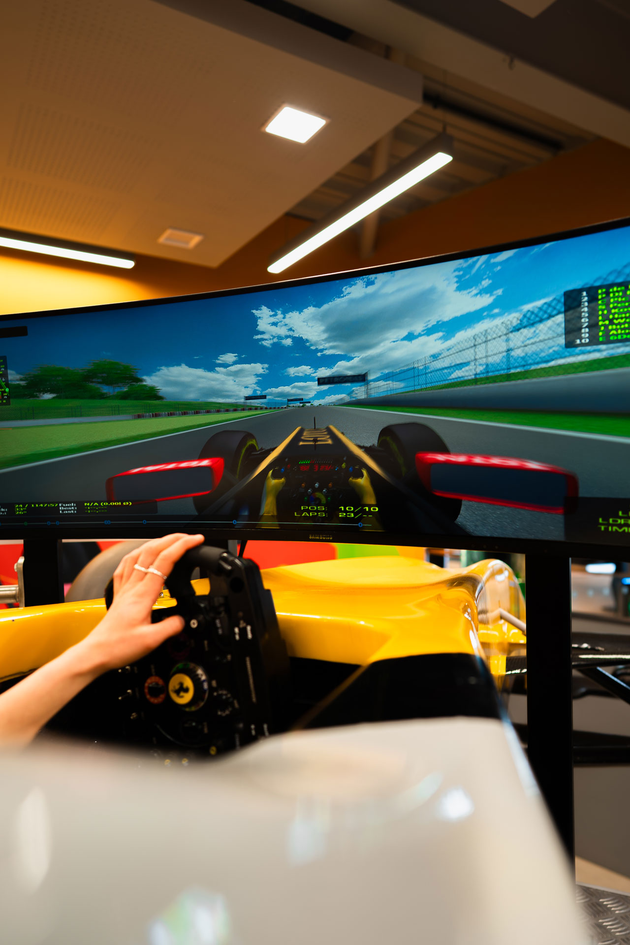 Person using a racing simulator with a realistic track view on a curved monitor.